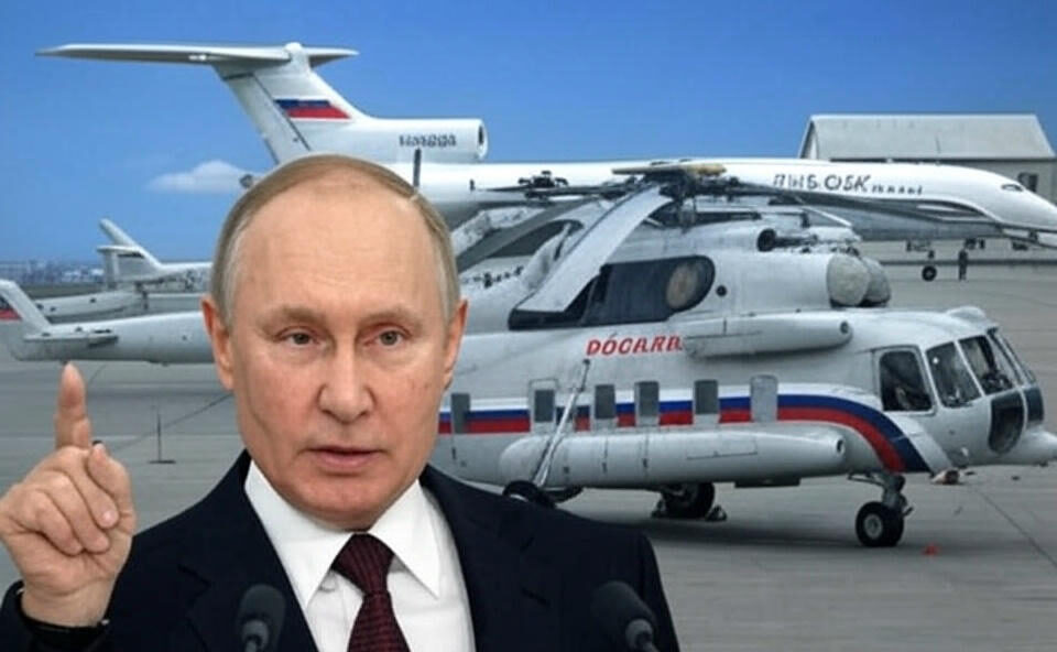 A dramatic scene featuring Vladimir Putin speaking at a podium with a raised finger, set against a backdrop of Russian helicopters on an airfield, with a faint drone silhouette and smoke trail symbolizing an alleged Ukrainian attack on May 20, 2025, in Kursk, under a bold yellow and black title reading "PUTIN’S CHOPPER UNDER UKRAINE’S STRIKE.