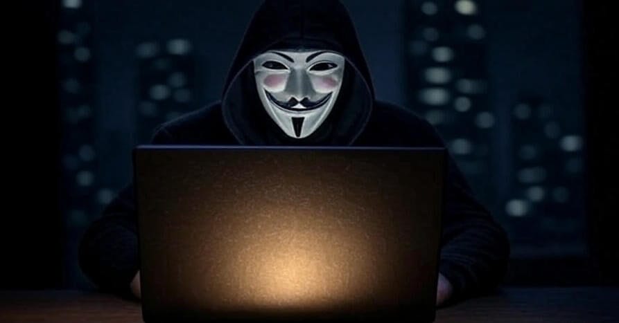 A masked hacker in a hood works a laptop at night in a city, plotting cyber attacks on U.S. banks as tensions rise.