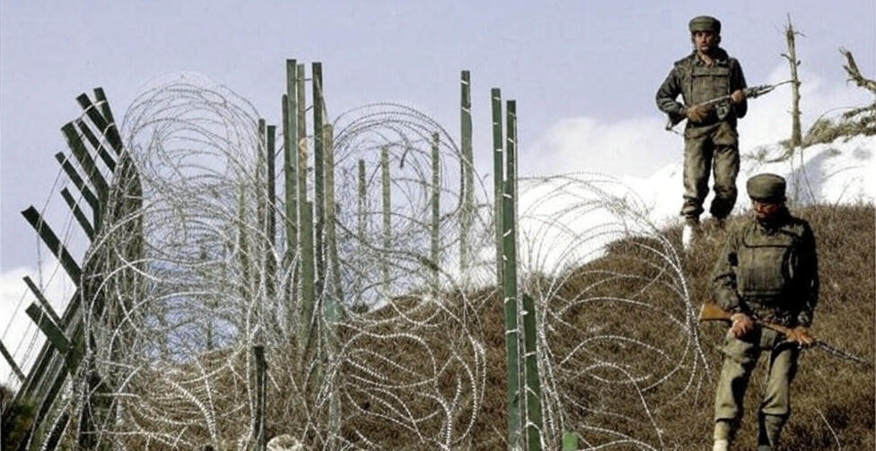 A tense scene of the India-Pakistan conflict on June 1, 2025, at 10:06 PM PKT, depicting two Indian soldiers in camouflage patrolling a rugged, snow-dusted hill near the Line of Control. They carry rifles and navigate through a dense barrier of barbed wire and wooden stakes, with a smoky, orange-tinged sky in the background symbolizing recent military tension. The image captures the heightened alert and human resolve amid the violent conflict inferno sparked by India’s alleged attack.