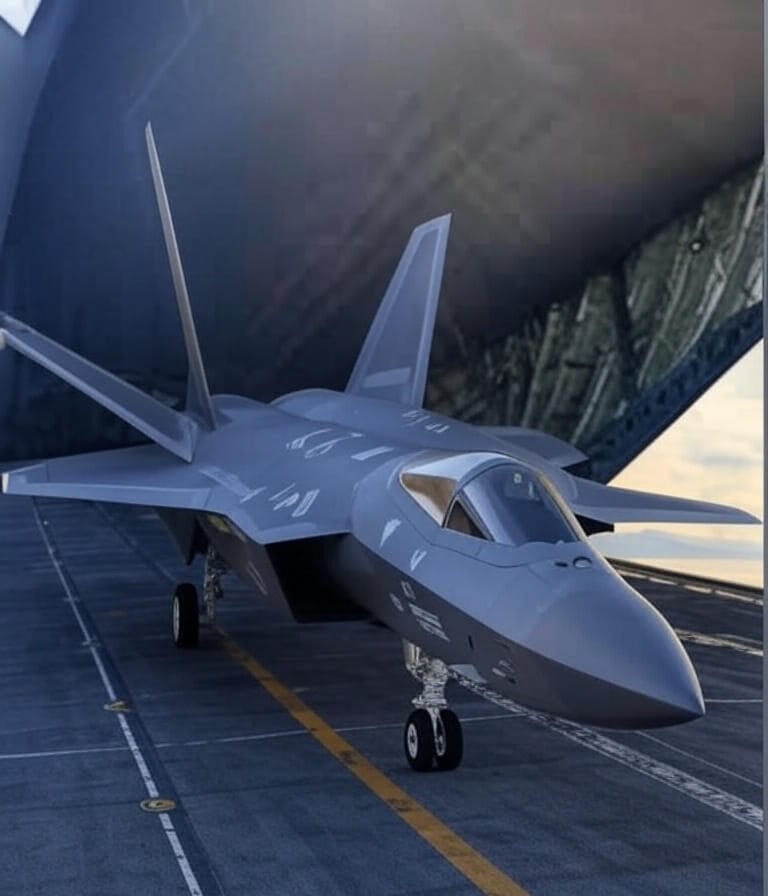 A British Royal Navy F-35B stealth fighter jet is being loaded into the cargo hold of a large military transport aircraft, likely a Royal Air Force C-17 Globemaster, at an airport tarmac. The jet is secured on a transport platform, with its nose and cockpit facing forward into the aircraft. The scene is set under a partly cloudy sky, with the transport aircraft's open rear ramp revealing additional cargo pallets covered in protective netting, indicating preparations for the jet's potential airlift following its emergency landing in Kerala, India, on June 14, 2025.