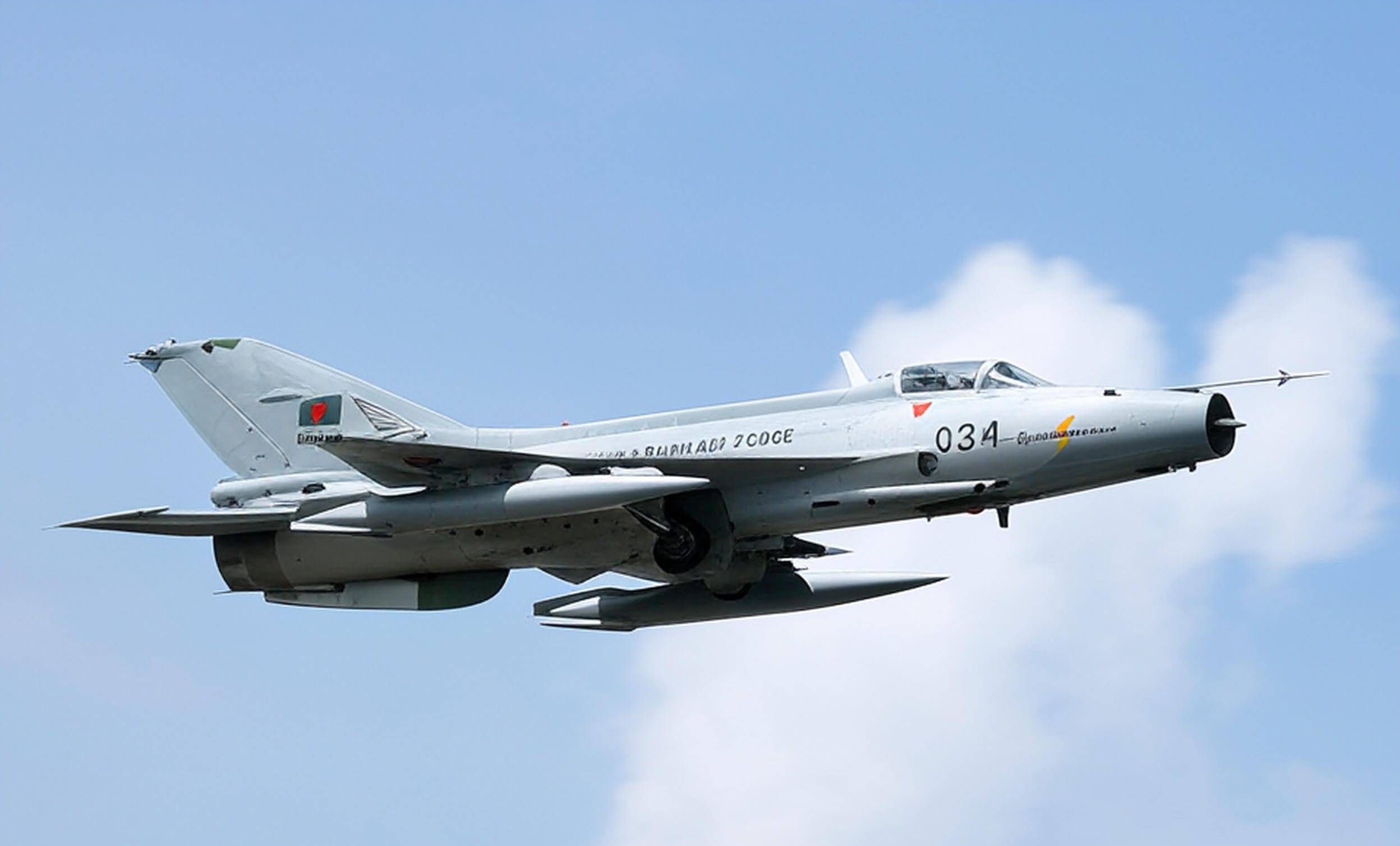 A Bangladesh Air Force F-7 BGI jet, marked with the national flag and identification number 934, flies against a clear blue sky, showcasing its sleek design and mounted weaponry, prior to the tragic crash on July 21, 2025, in Dhaka.