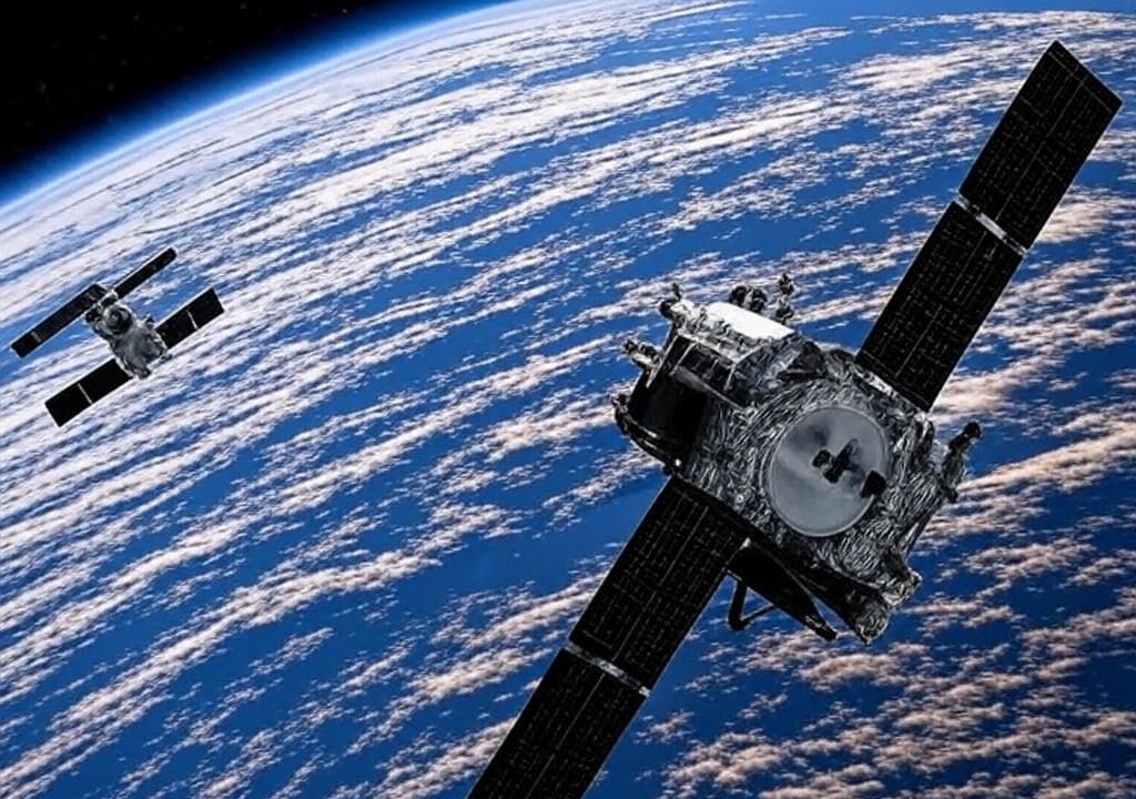 The image depicts two satellites orbiting Earth, with one prominently in the foreground featuring large solar panels and a detailed body, while the other is visible in the background. The scene showcases a view of Earth's cloud-covered surface and the curvature of the planet against the backdrop of space, highlighting the satellites' operational environment.