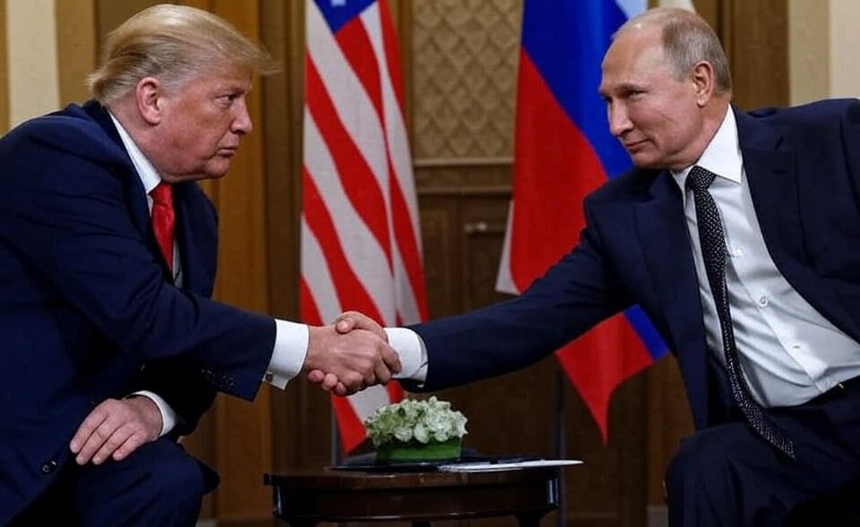 Two individuals in formal suits shaking hands across a small table with a floral arrangement, with the American and Russian flags in the background.