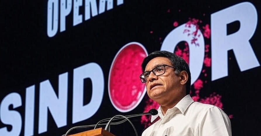 A person in a white shirt stands at a podium with microphones, speaking in front of a large screen displaying the text "OPERATION SINDOOR" with a red circular design and pink splashes, set against a dark background.