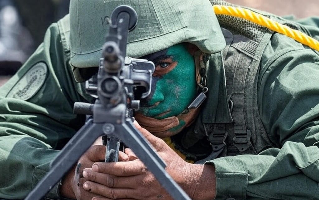 A Venezuelan soldier in green camouflage and face paint lies prone, aiming a mounted machine gun during a training exercise, symbolizing Caracas' vigilance amid claims of capturing CIA-backed mercenaries plotting a false-flag attack in the Caribbean on October 27, 2025.