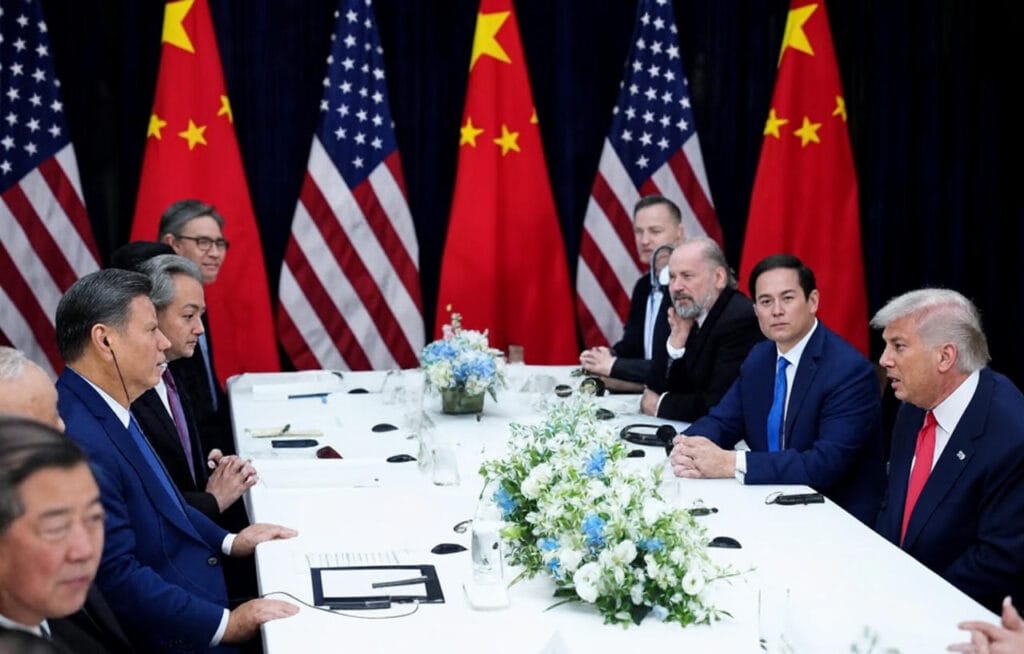 U.S. President Donald Trump and Chinese President Xi Jinping lead high-level delegations seated across a white conference table adorned with floral centerpieces and alternating U.S. and Chinese flags, during closed-door bilateral negotiations at the APEC summit in Busan, South Korea, on October 30, 2025, resulting in tariff reductions, soybean import commitments, and a one-year pause on rare earth export restrictions.