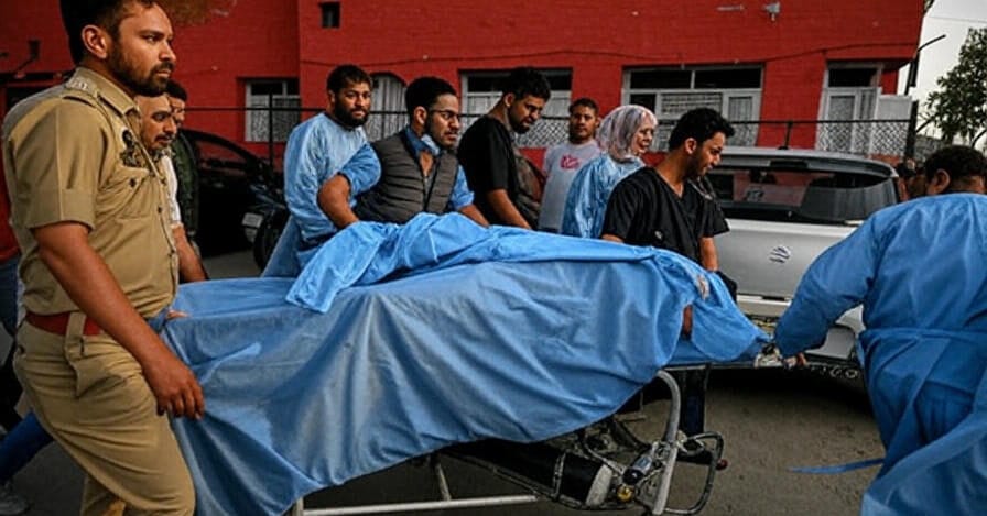 Medical personnel and a police officer rush a covered body on a stretcher toward a hospital entrance following the deadly suicide bombing outside the district court complex in Islamabad on November 11, 2025, as shocked bystanders look on against the red-brick building backdrop.